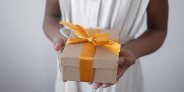 person holding a gift box with a decorative yellow ribbon.