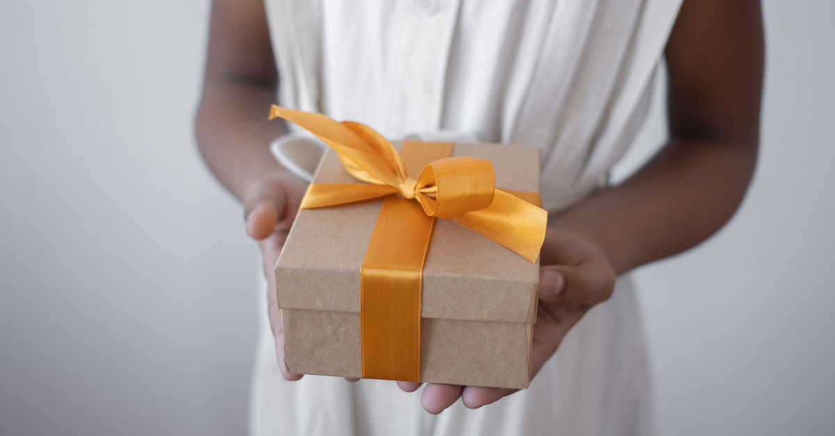 person holding out a gift box tied with a ribbon.