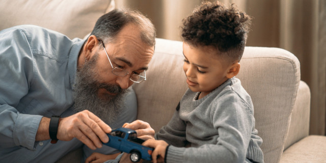 man with beard playing with a toy truck with a short-haired child.