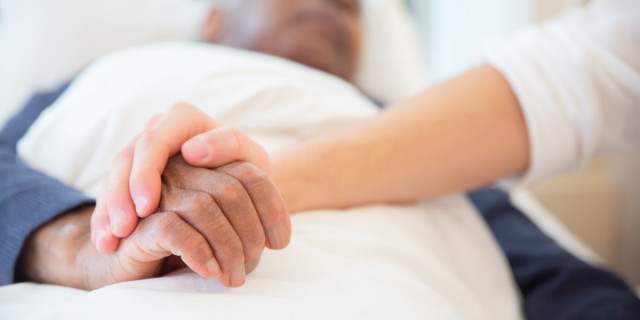 young person's hand on an old person's hand resting on a bed.