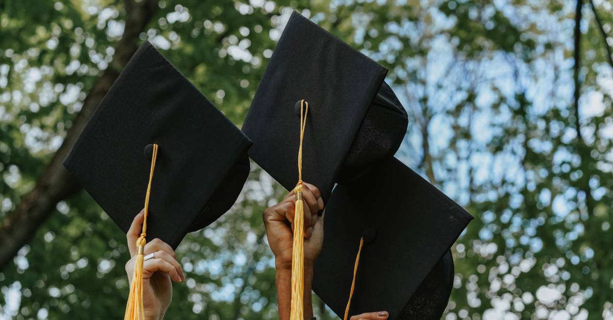 hands holding graduation caps in the air.