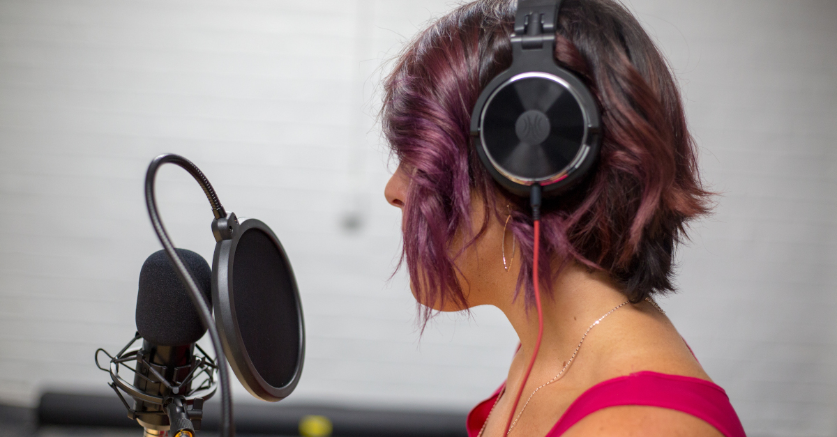 person with purple hair, wearing headphones and speaking into a microphone.