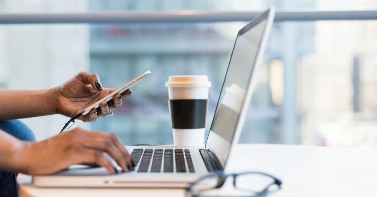 detail of a person using a smartphone and a laptop.