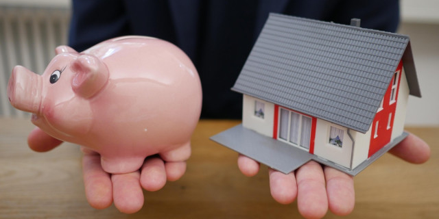 close-up of hands holding a piggy bank and a model house.