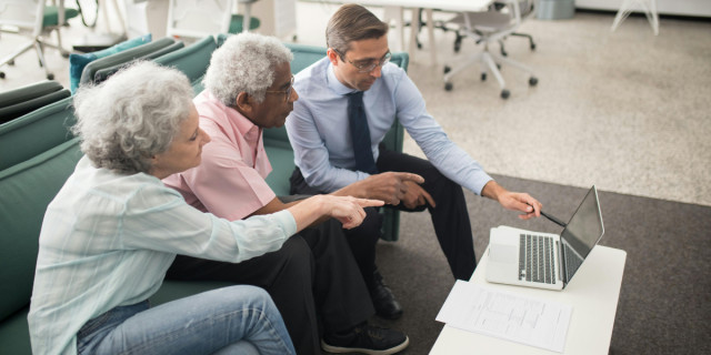 Older couple sitting on couch with younger business person, looking at a laptop.