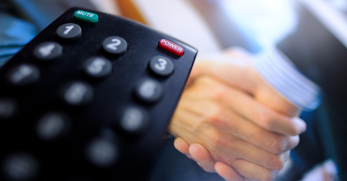 a TV remote in front of a blurry image of a handshake.